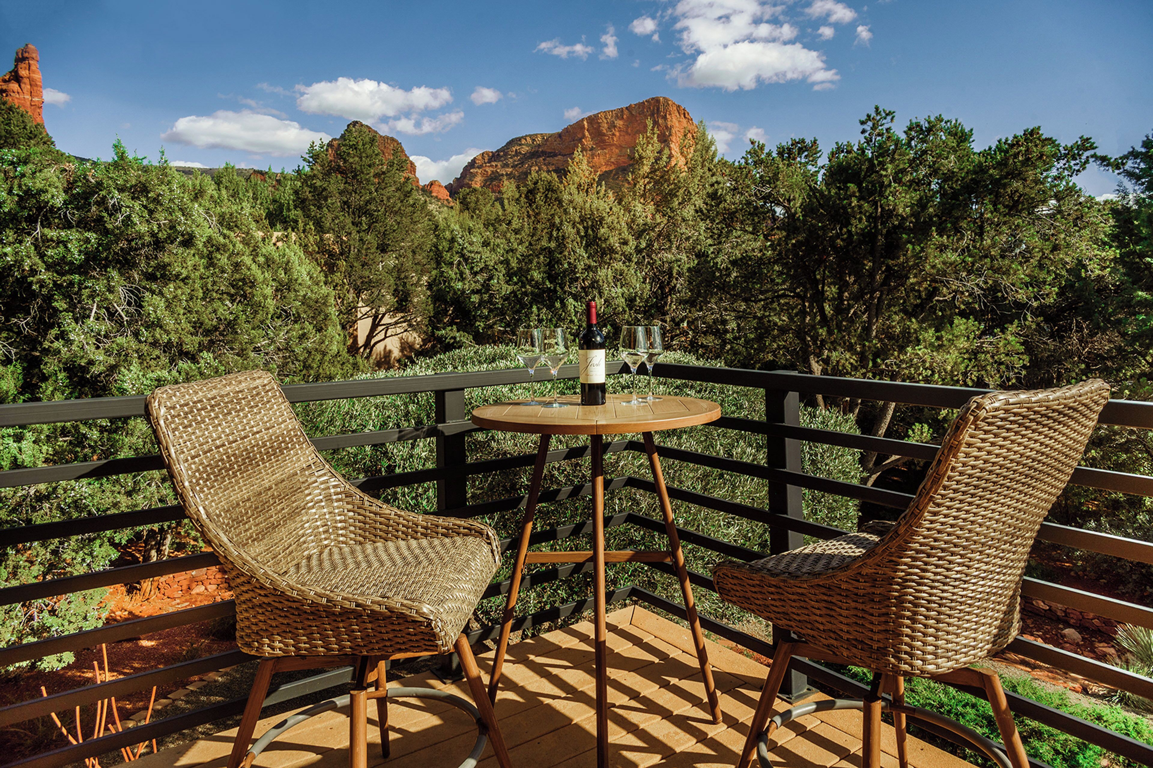 Ein Balkon mit Korbstühlen und einem Tisch, mit Blick auf eine bewaldete Landschaft und Berge im Hintergrund.