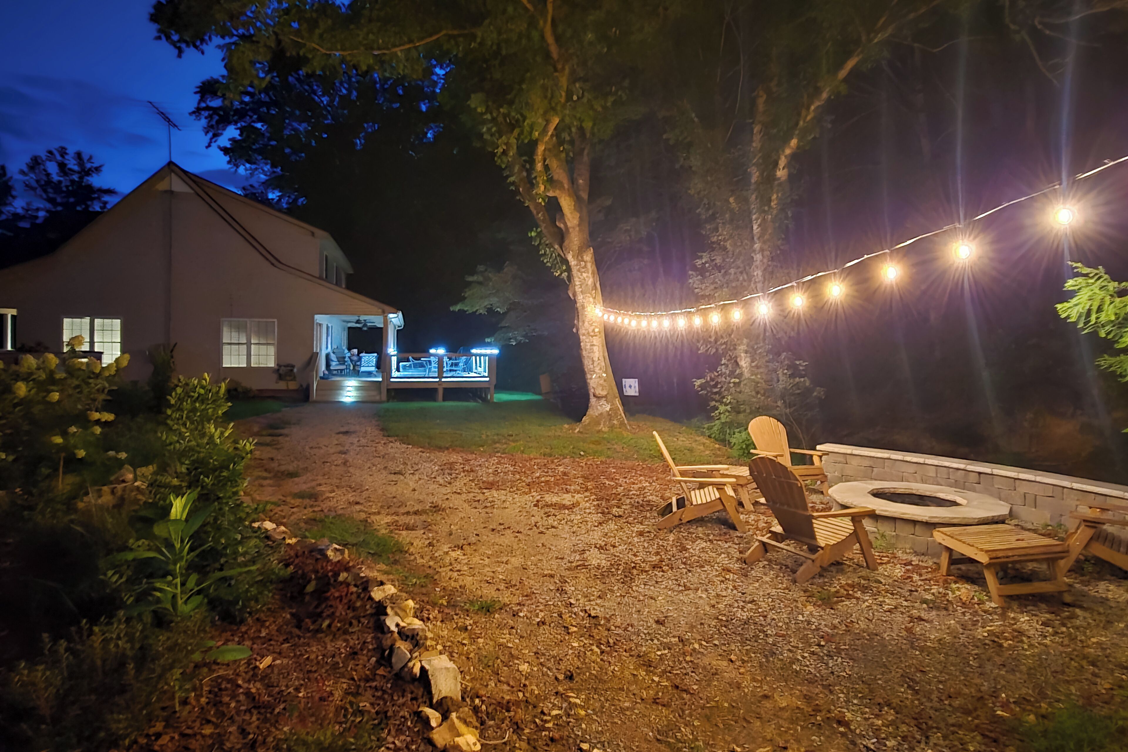 Un patio trasero con un hogar, sillas de madera y luces colgantes.