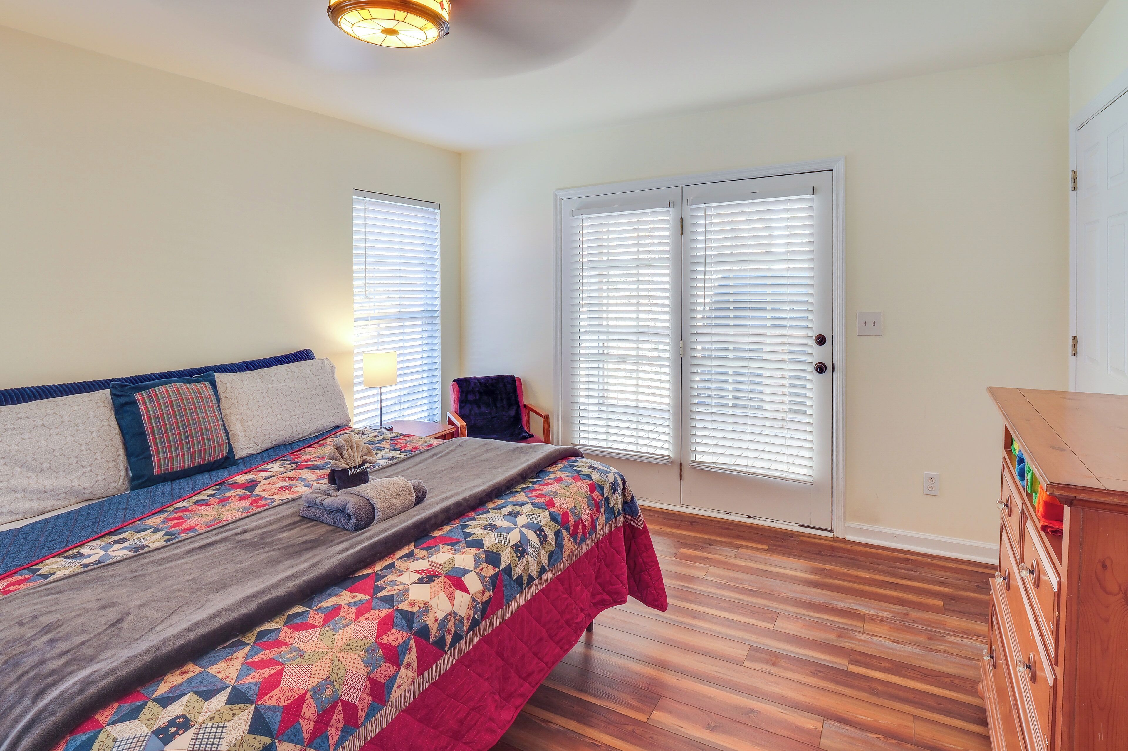 Une chambre à coucher avec un grand lit, une commode, une chaise et une porte équipée de stores.