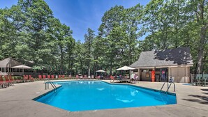 A rectangular swimming pool with a concrete deck, surrounded by red and green lounge chairs, and shaded by umbrellas. - 1st-floor Wintergreen Resort Condo w/ Balcony (Nellysford)