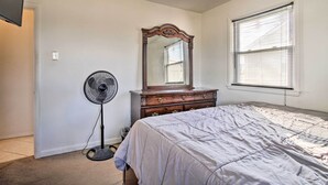 A bedroom with a bed, dresser, mirror, fan, and window.