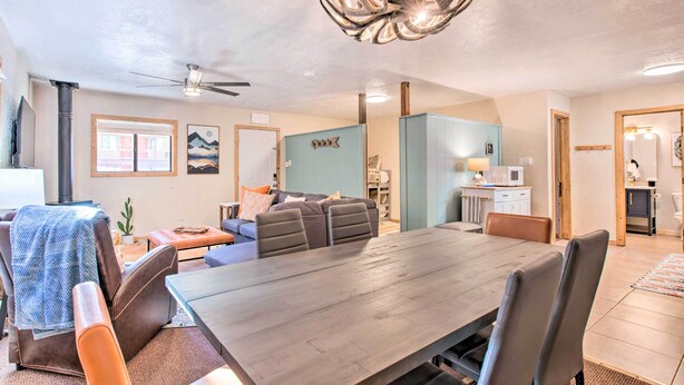 A spacious living area with a large dining table, comfortable seating, a ceiling fan, and a modern kitchen in the background.