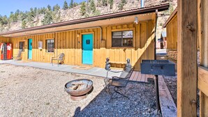 A wooden cabin with a blue door, a fire pit, and two chairs.