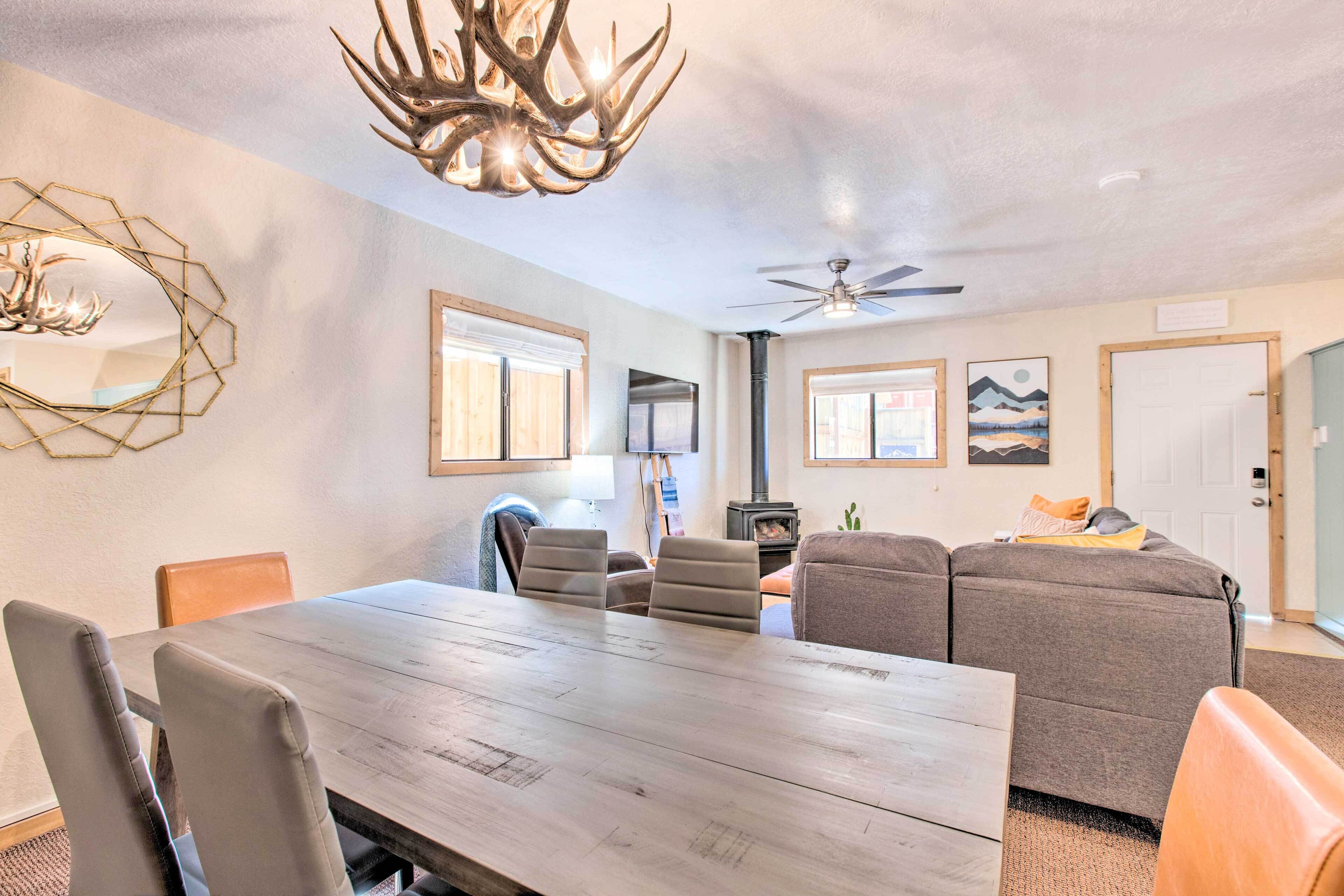 A dining area with a wooden table and chairs, a ceiling fan, and a decorative antler chandelier.