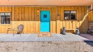 A wooden cabin with a turquoise door, a bench, and two bear statues on the porch.
