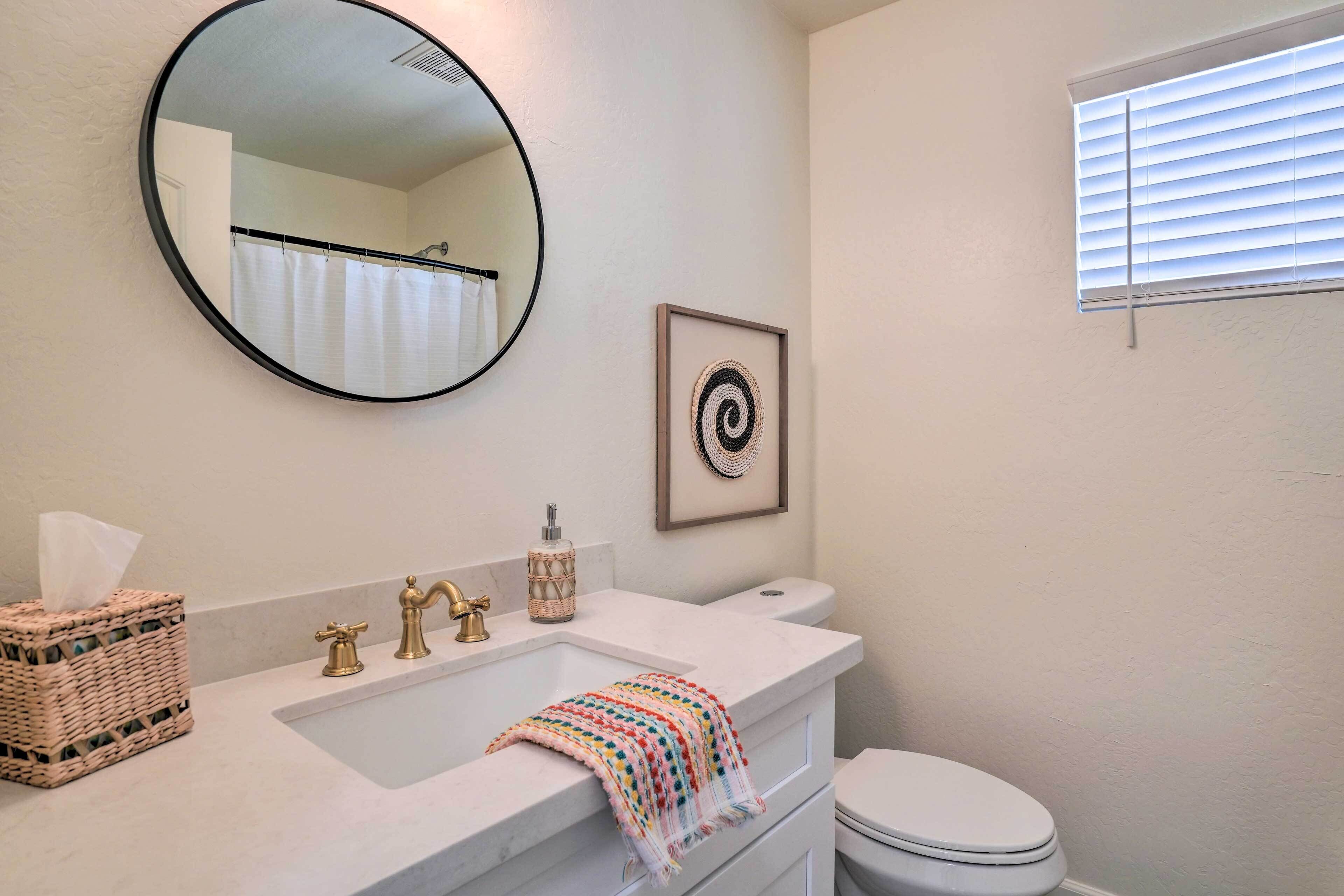 A bathroom with a round mirror, a sink with a towel, a toilet, and a framed picture on the wall.
