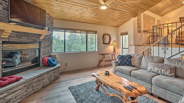 Ein geräumiges Wohnzimmer mit Kamin aus Stein, einem großen Flachbildfernseher, einem Holztisch und einem grauen Sofa mit einem Kissen mit dem Aufdruck 'home'.