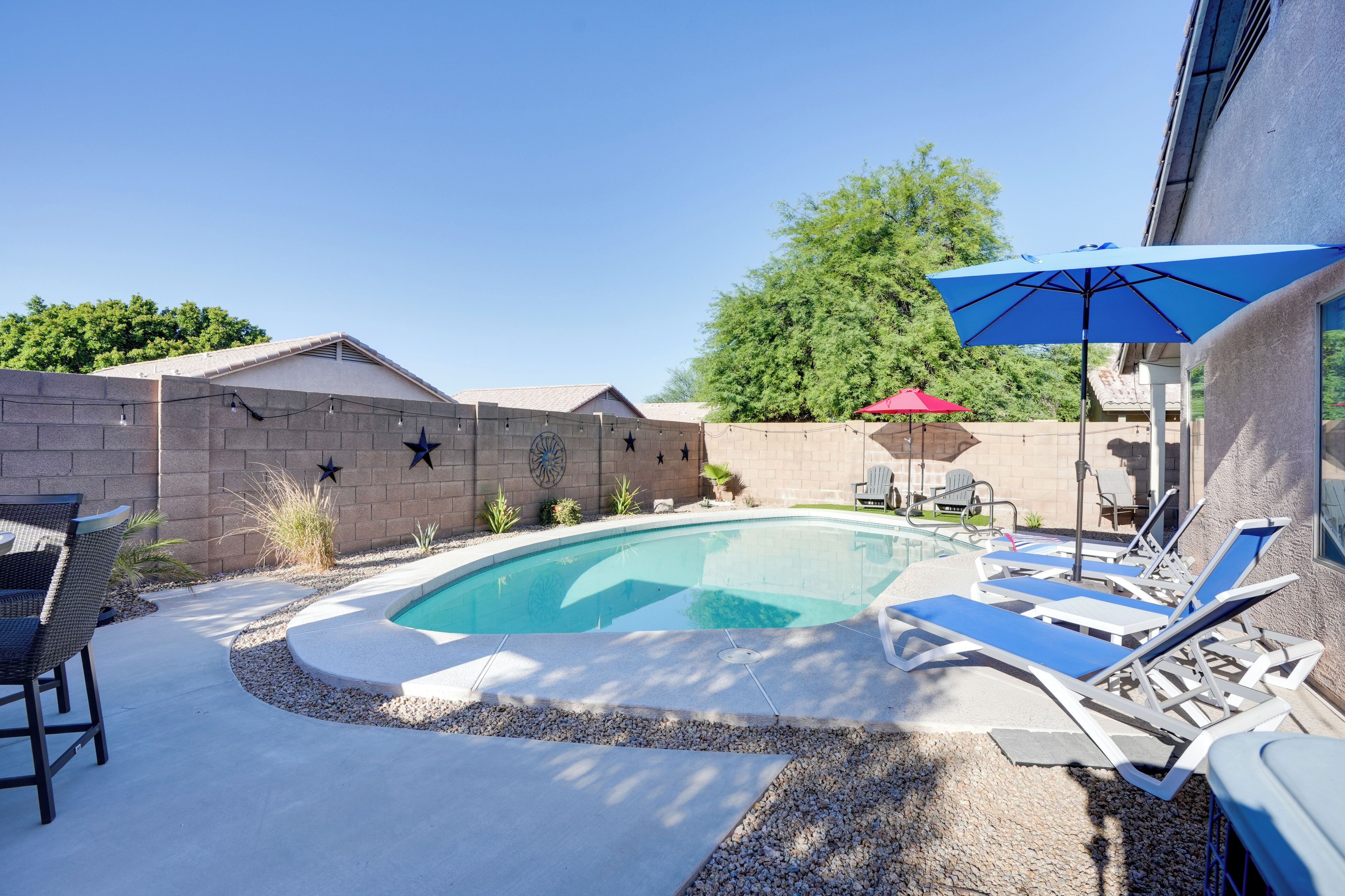 A backyard with a swimming pool, lounge chairs, and a red umbrella.