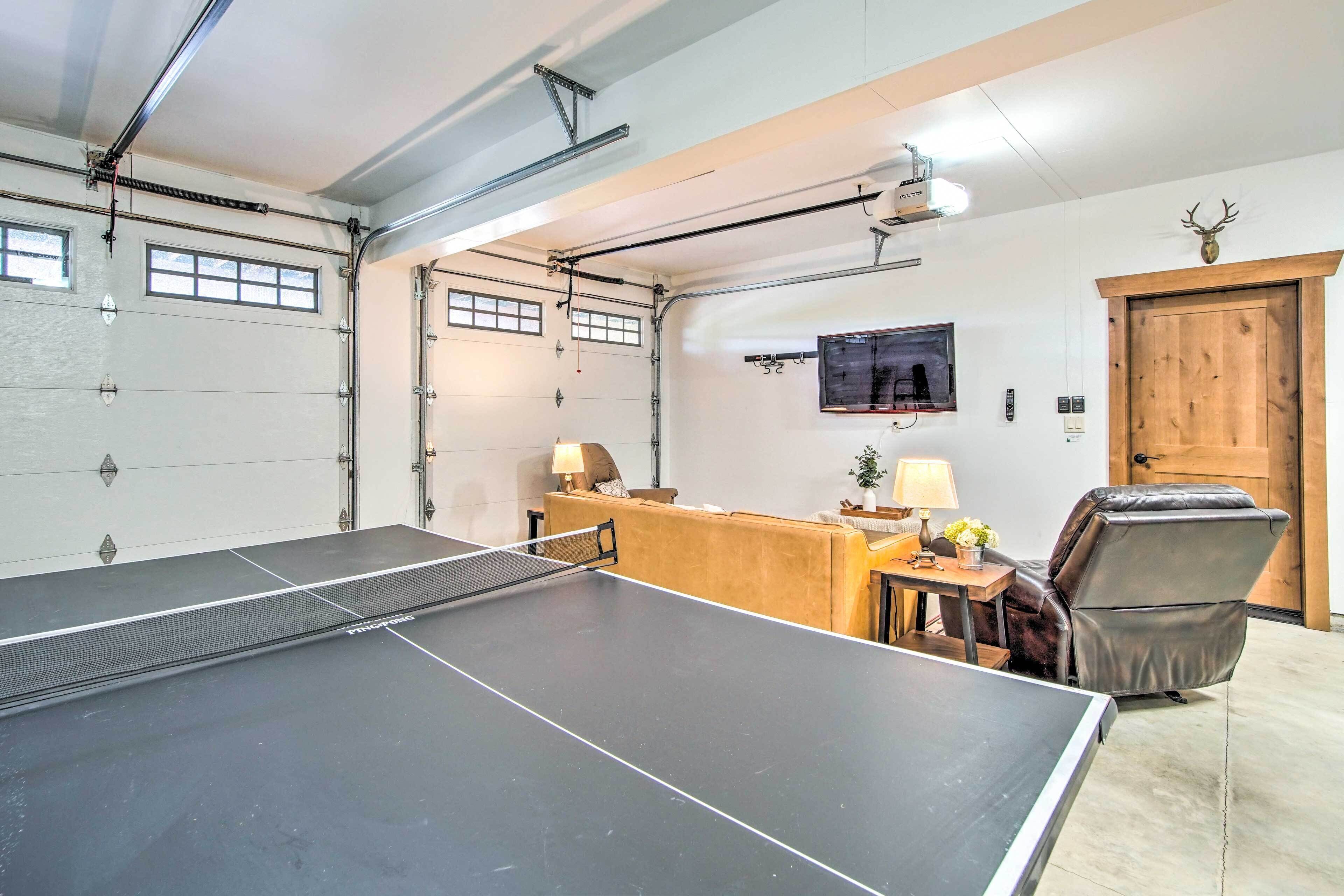 Una mesa de ping pong en una habitación con una puerta de madera, un televisor montado y un sillón de cuero.