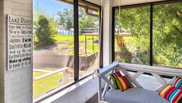 A room with a large window overlooking a grassy area, a white brick wall, and a white bed with colorful pillows. - Lakefront Family Home w/ Boat Dock + Slip in Texas (Trinidad)