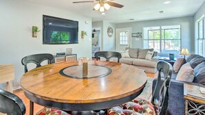 A spacious living room with a round wooden dining table, a ceiling fan, a flat-screen TV mounted on the wall, and a large window providing natural light. - Lakefront Family Home w/ Boat Dock + Slip in Texas (Trinidad)