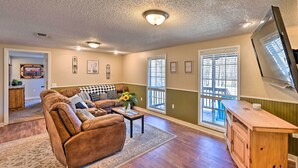A spacious living room with a brown leather sofa, a wooden coffee table, and a TV mounted on the wall. - 'whispering Oaks' Broken Bow Cottage Near Hiking! (Broken Bow)