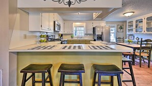 A kitchen with white cabinets, a central island with stools, a decorative ceiling piece, and a view of the dining area. - 'whispering Oaks' Broken Bow Cottage Near Hiking! (Broken Bow)