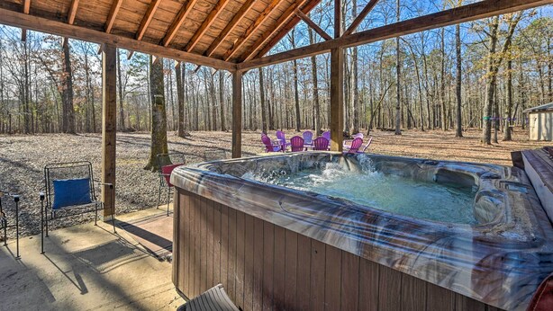 A wooden deck with a hot tub, surrounded by trees and outdoor chairs. - 'whispering Oaks' Broken Bow Cottage Near Hiking! (Broken Bow)