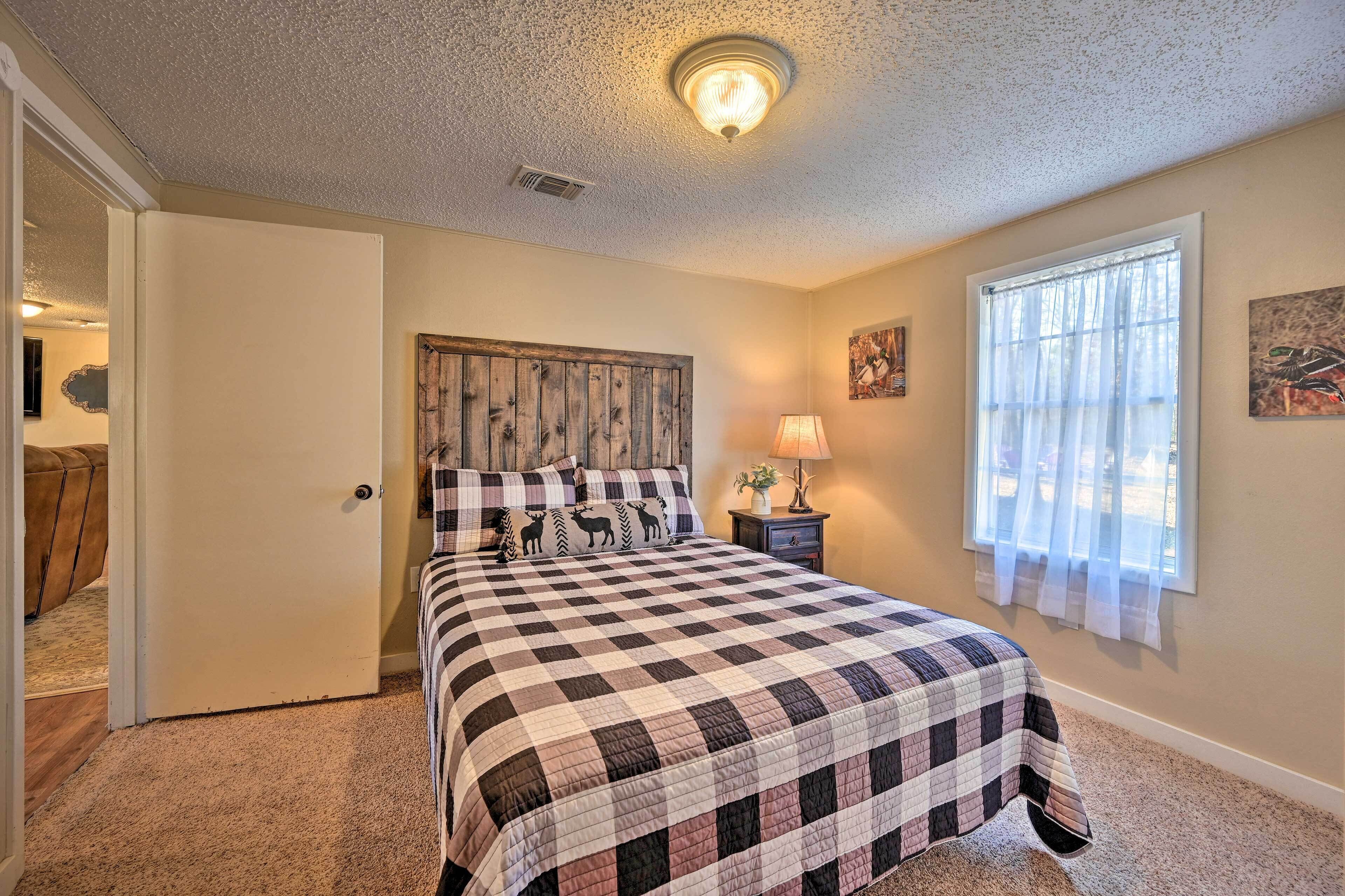 A bedroom with a checkered bedspread, a wooden headboard, a bedside lamp, and a window with sheer curtains.