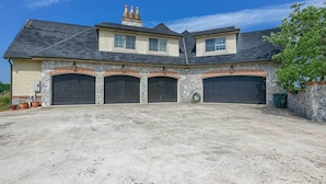 A two-story house with a stone facade, three garage doors, and a large driveway.