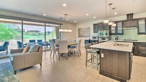 A modern kitchen with a central island, dining area with chairs, and large windows offering a view of greenery. - Scottsdale Condo w/ Resort-style Perks! (Scottsdale)