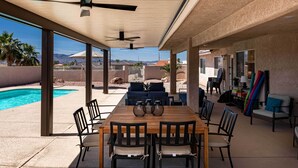 An outdoor patio with a wooden table and chairs, a pool, and a covered seating area with a view of the mountains.