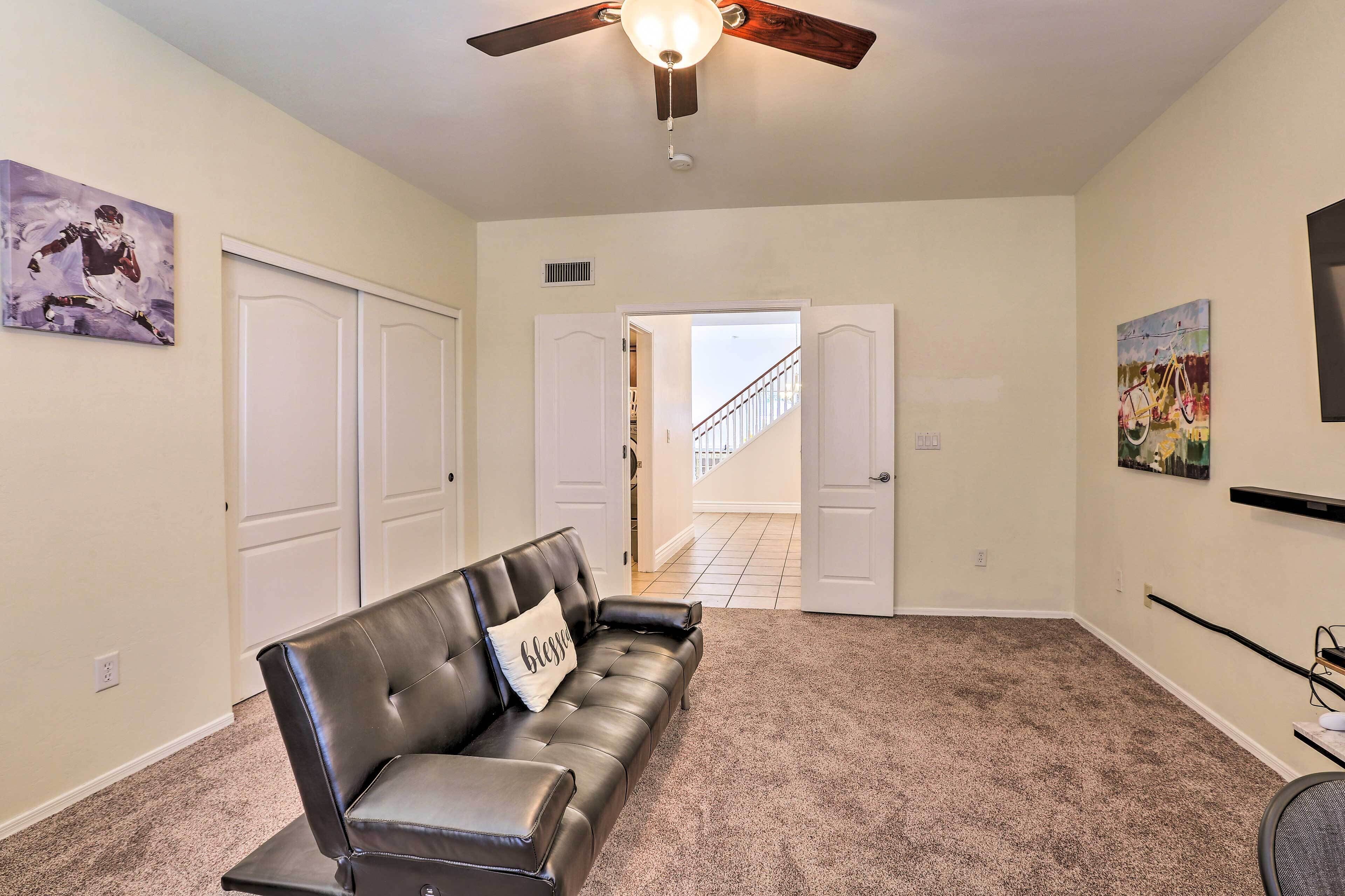 A living room with a black leather sofa, a ceiling fan, and a door leading to a staircase.