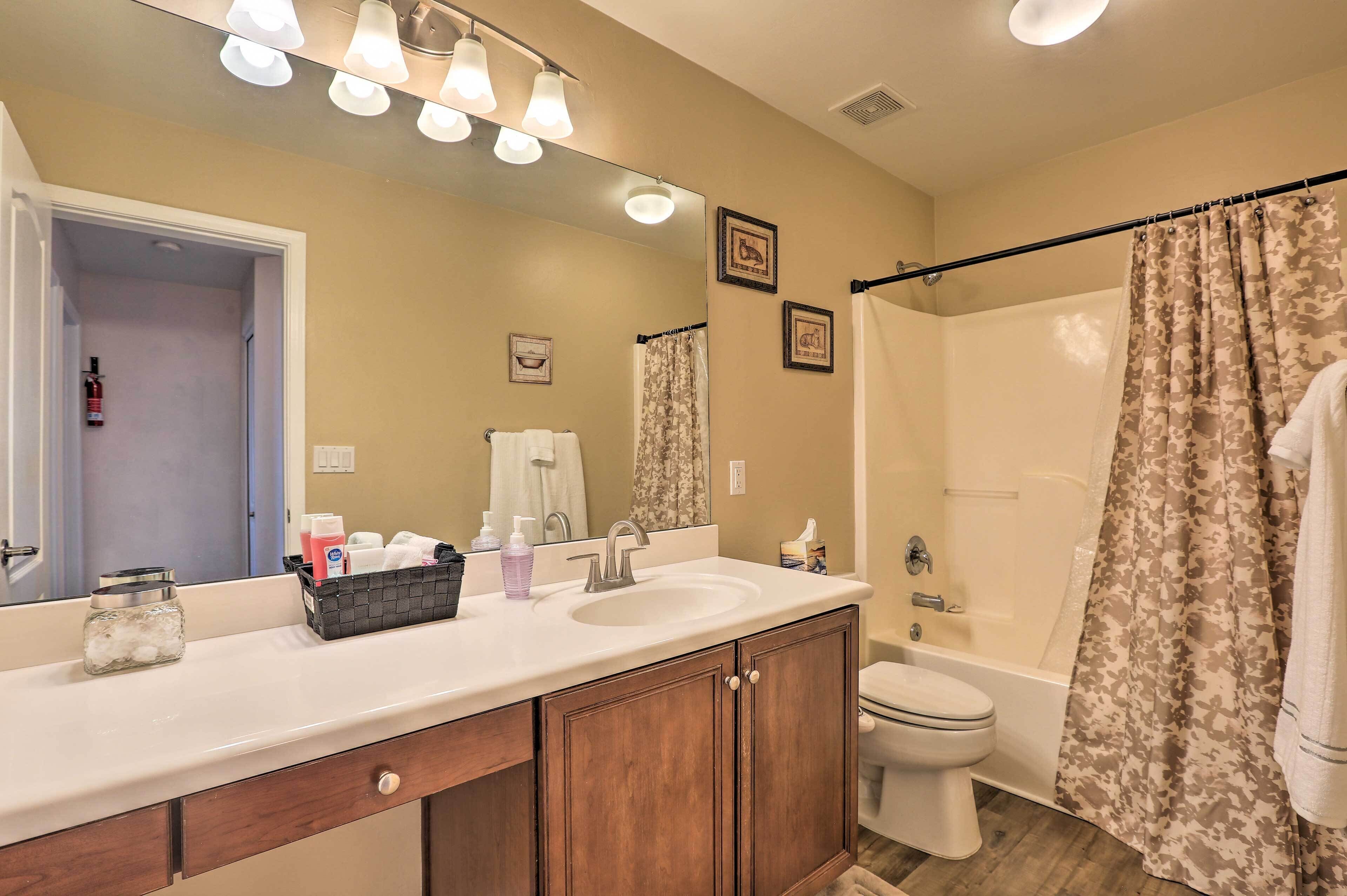 Une salle de bain avec un lavabo blanc, un miroir et un meuble-lavabo, une douche avec un rideau à motifs floraux et des toilettes.