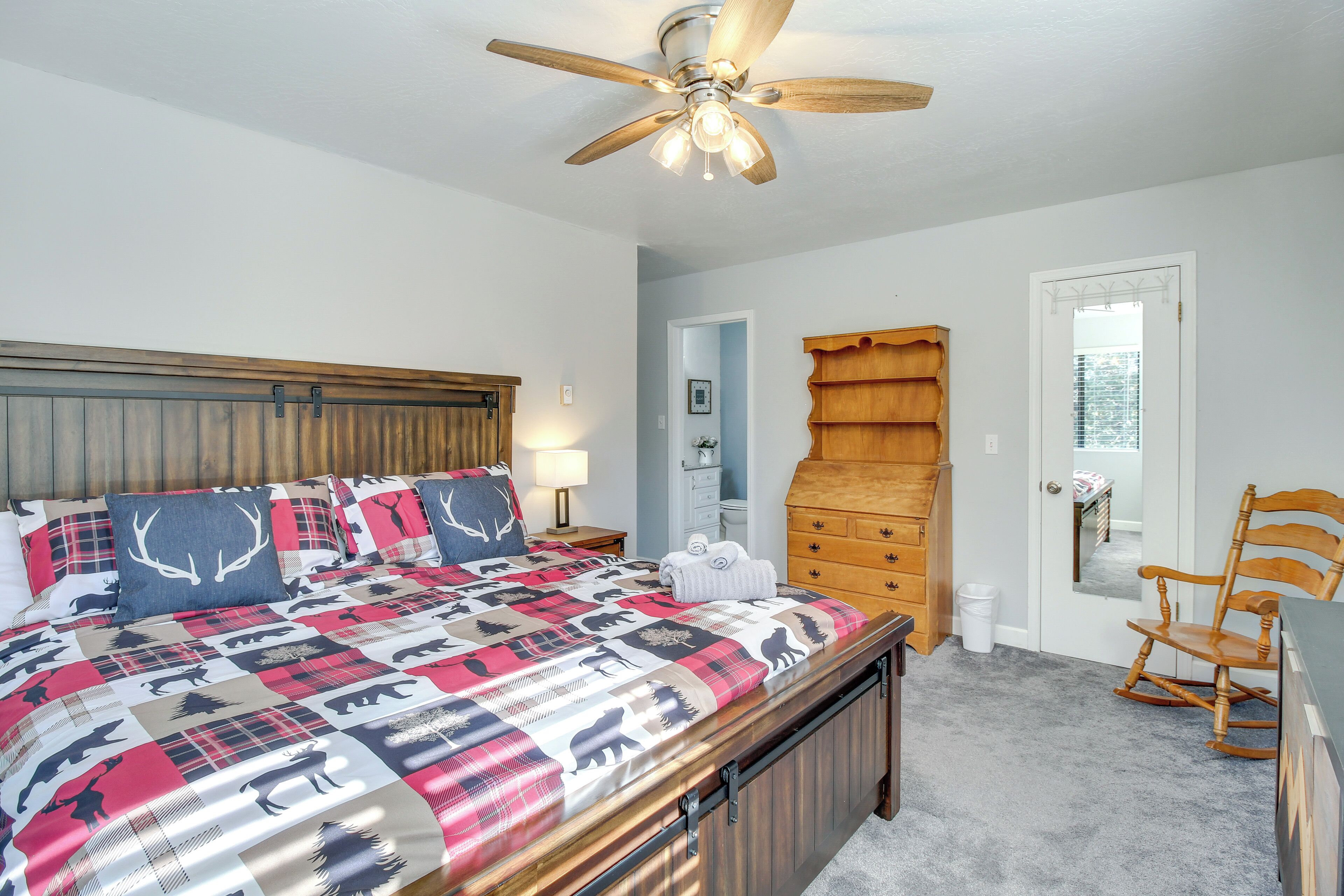 Une chambre à coucher comprenant un lit, un ventilateur de plafond, une commode, un fauteuil à bascule et une porte donnant sur une autre pièce.