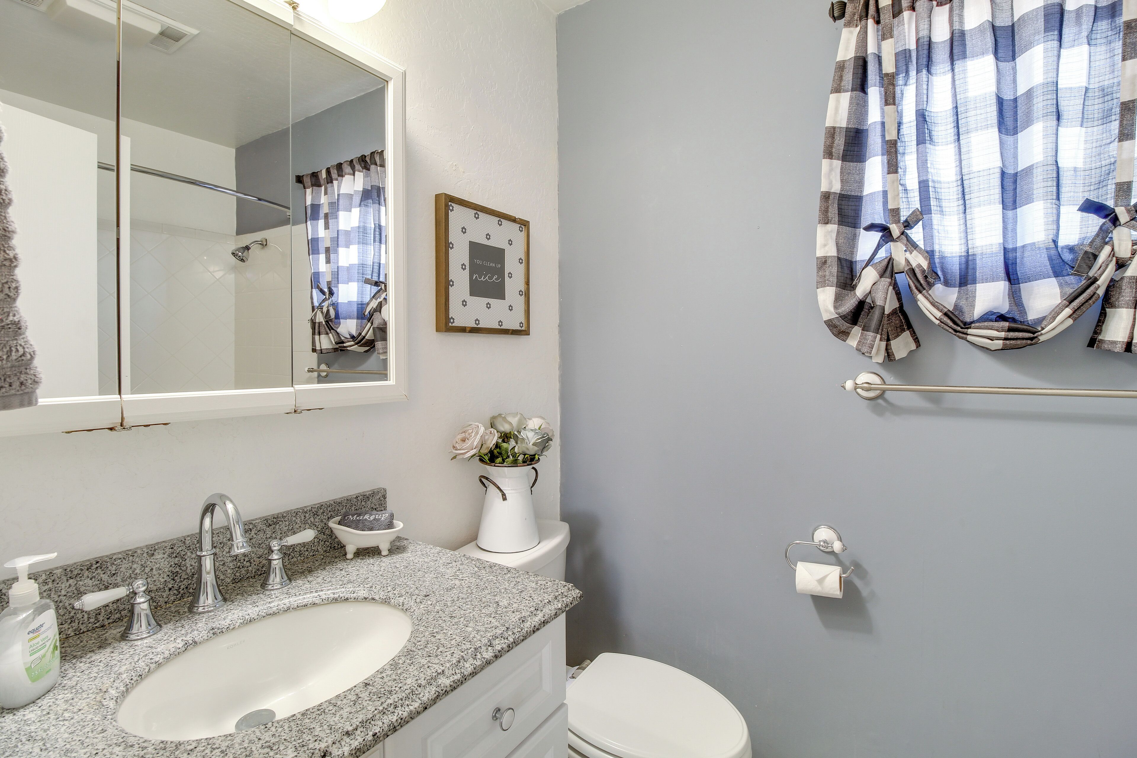 Un baño con lavabo de granito, inodoro blanco y espejo sobre el lavabo.