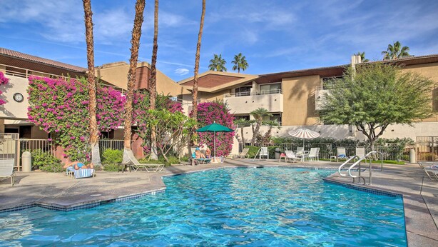 A swimming pool with lounge chairs and umbrellas, surrounded by palm trees and a building with balconies. - Walk to Dtwn Palm Springs: Condo w/ Pool Access (Palm Springs)