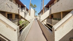 A corridor with a central walkway flanked by buildings with balconies, palm trees, and a clear blue sky. - Walk to Dtwn Palm Springs: Condo w/ Pool Access (Palm Springs)
