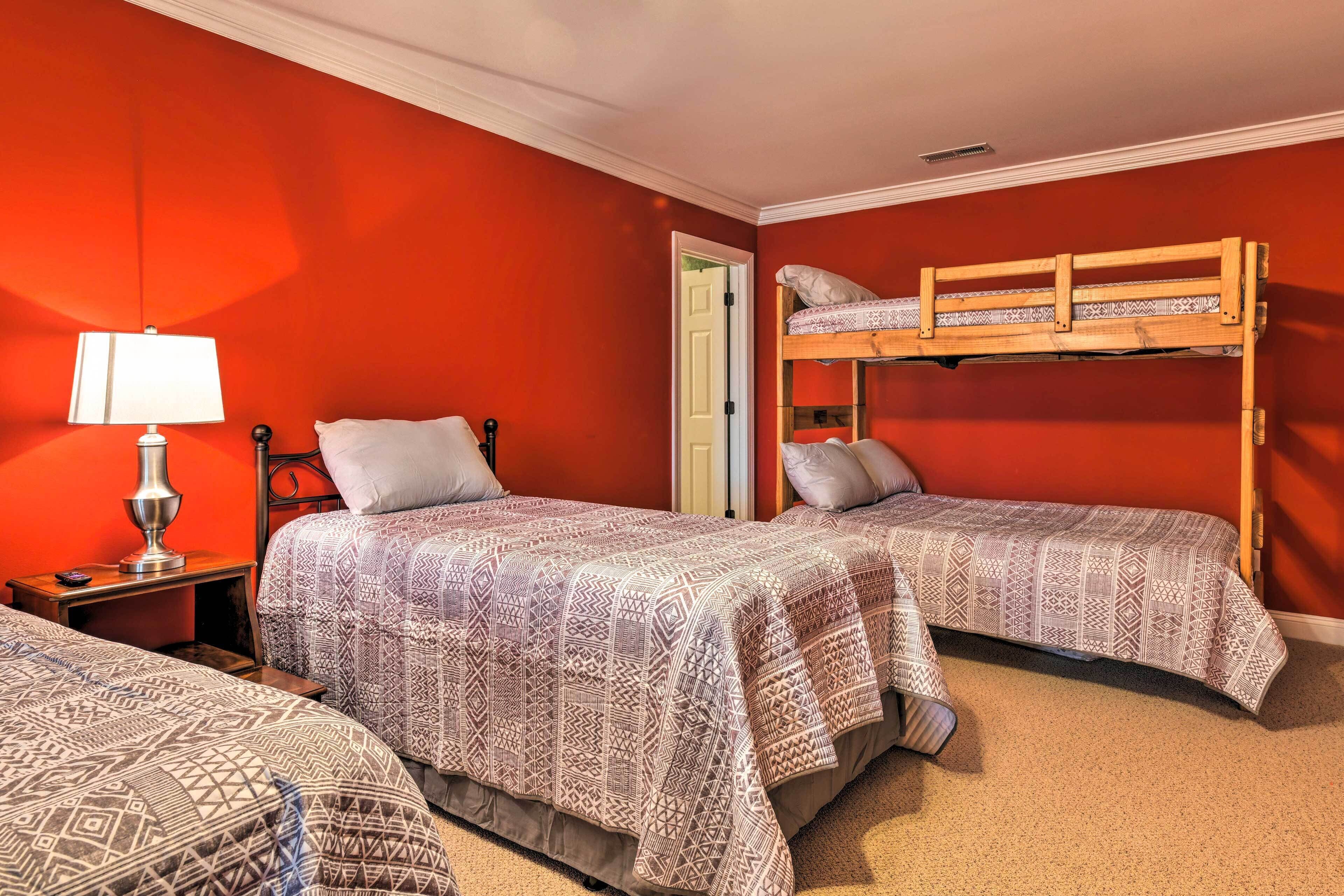 A room with two beds, each with patterned bedding, a bedside lamp, and a wooden bunk bed.