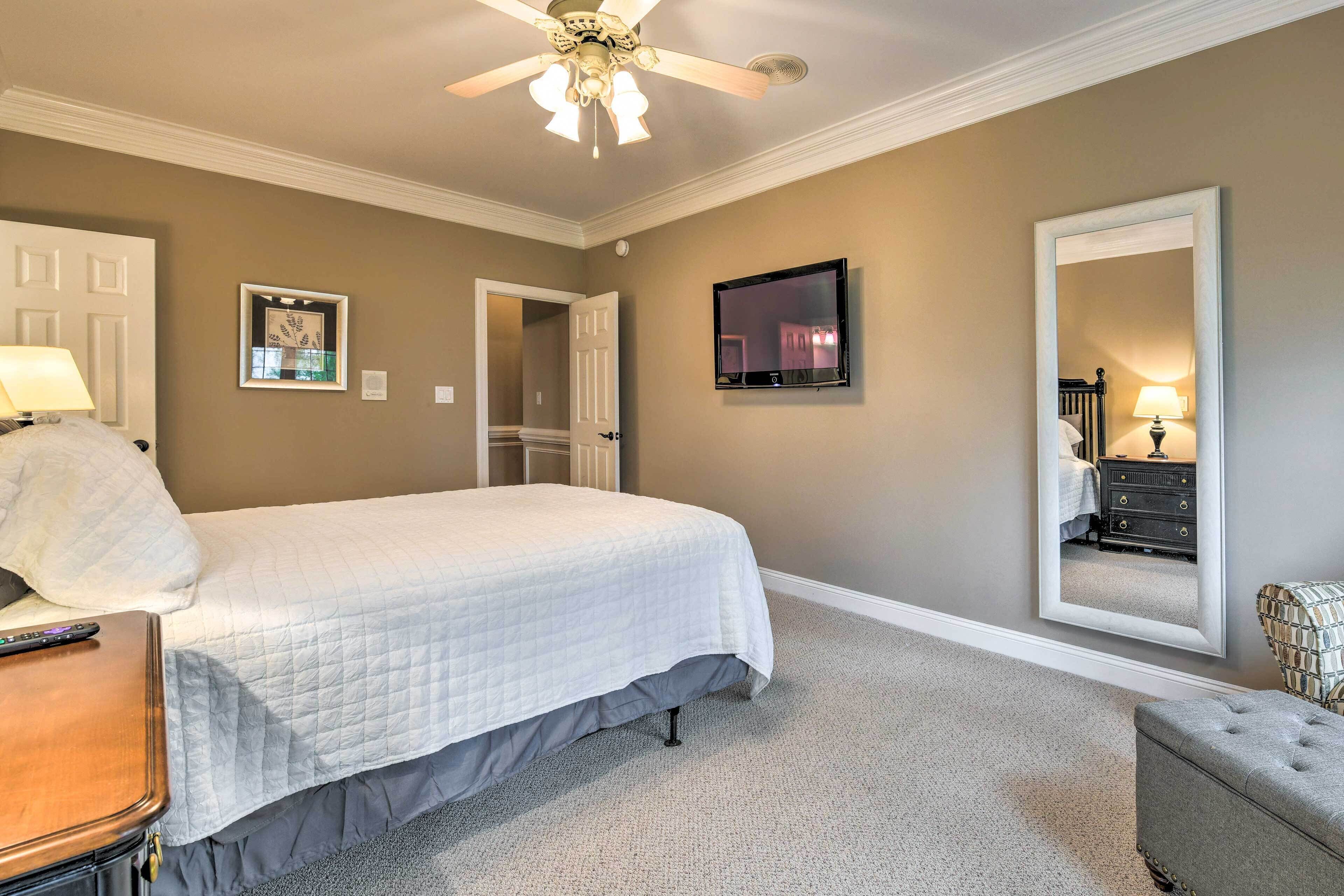 A bedroom with a bed, a ceiling fan, a TV, a mirror, and a dresser.
