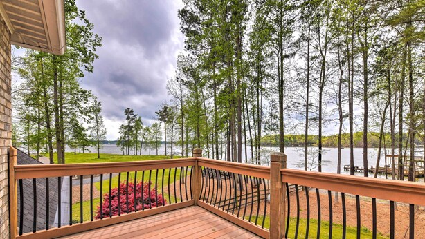 A wooden deck with a metal railing overlooking a lake and trees.