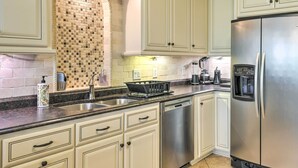 A kitchen with white cabinets, a stainless steel refrigerator, a sink, and a tiled backsplash.