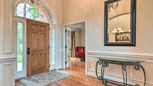 A hallway with a wooden door, a glass-top console table, and a large mirror on the wall.