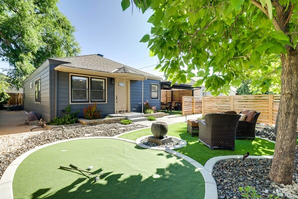 Una casa con patio trasero que incluye un campo de práctica de golf, mobiliario exterior y una valla de madera.