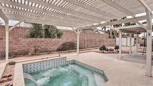 A covered outdoor swimming pool with a pergola overhead, surrounded by a brick wall and a patio area.