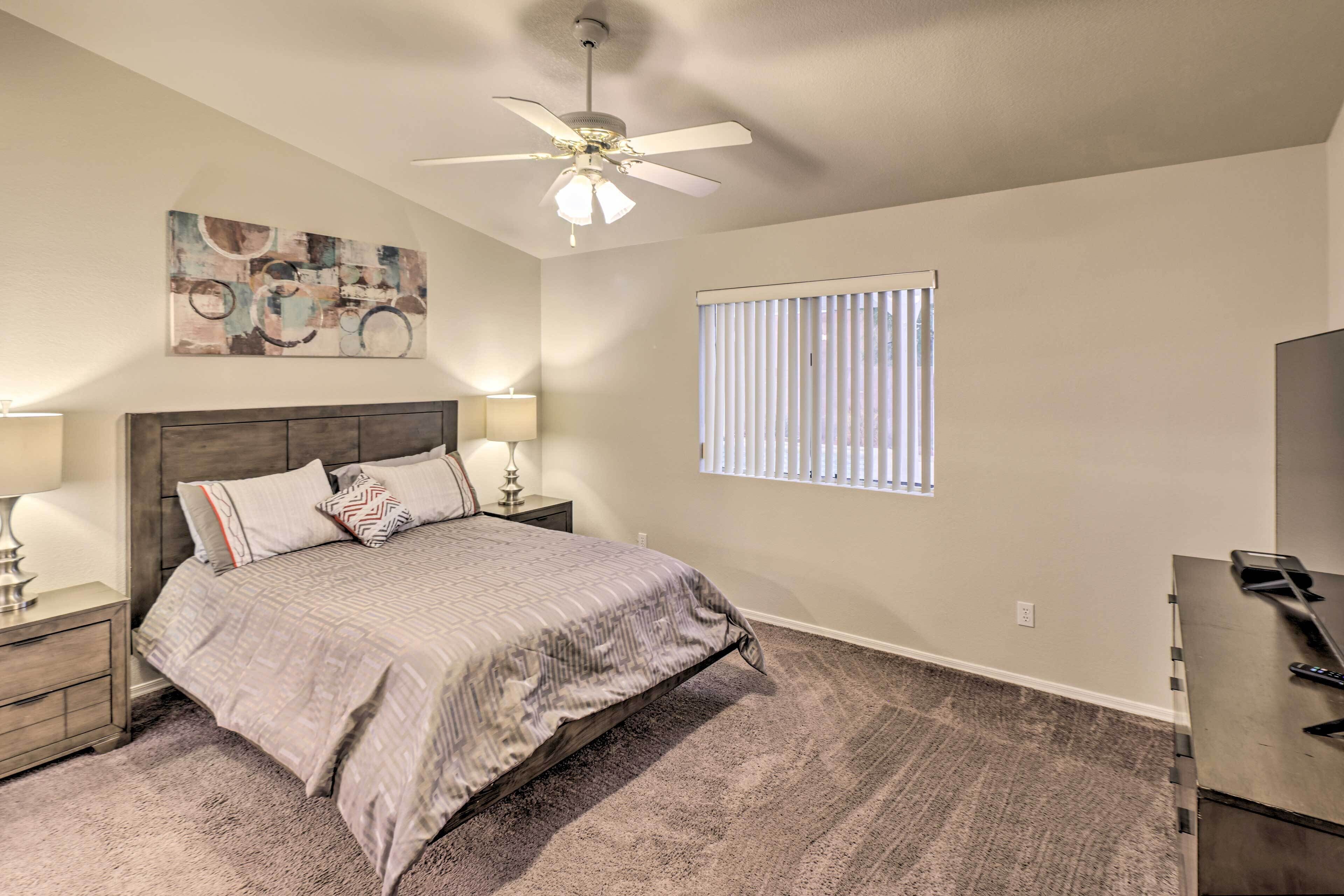A bedroom with a bed, nightstands, a ceiling fan, a window with blinds, and a TV stand.