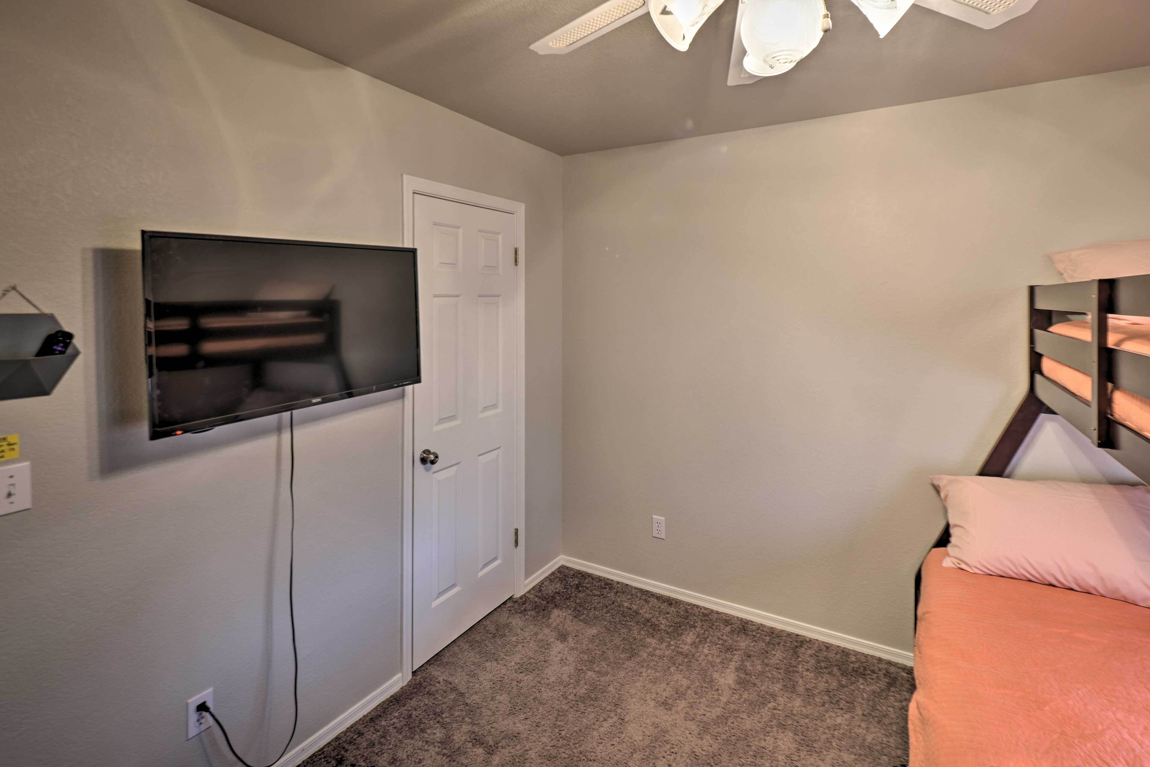 Une chambre à coucher avec un lit, un téléviseur fixé au mur, une porte et un ventilateur de plafond.