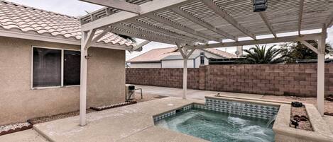 A covered outdoor area with a swimming pool, a pergola, and a brick wall.