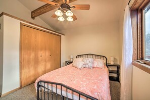 Un dormitorio con cama, armario de madera, ventilador de techo y ventana con cortinas.