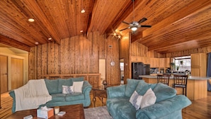 A spacious living area with two teal sofas, wooden ceiling, and a kitchen area with wooden cabinets and a bar. - Grand Escape w/ Deck, Game Room, Nature View! (Brooklyn)