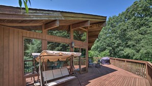 A wooden deck with a swing chair and umbrella, glass doors, and a view of trees. - Grand Escape w/ Deck, Game Room, Nature View! (Brooklyn)