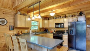 A wooden cabin kitchen with a central island, wooden cabinets, a refrigerator, and hanging pendant lights. - Lakefront Hazelhurst Cabin: Dock & Pool Table (Hazelhurst)