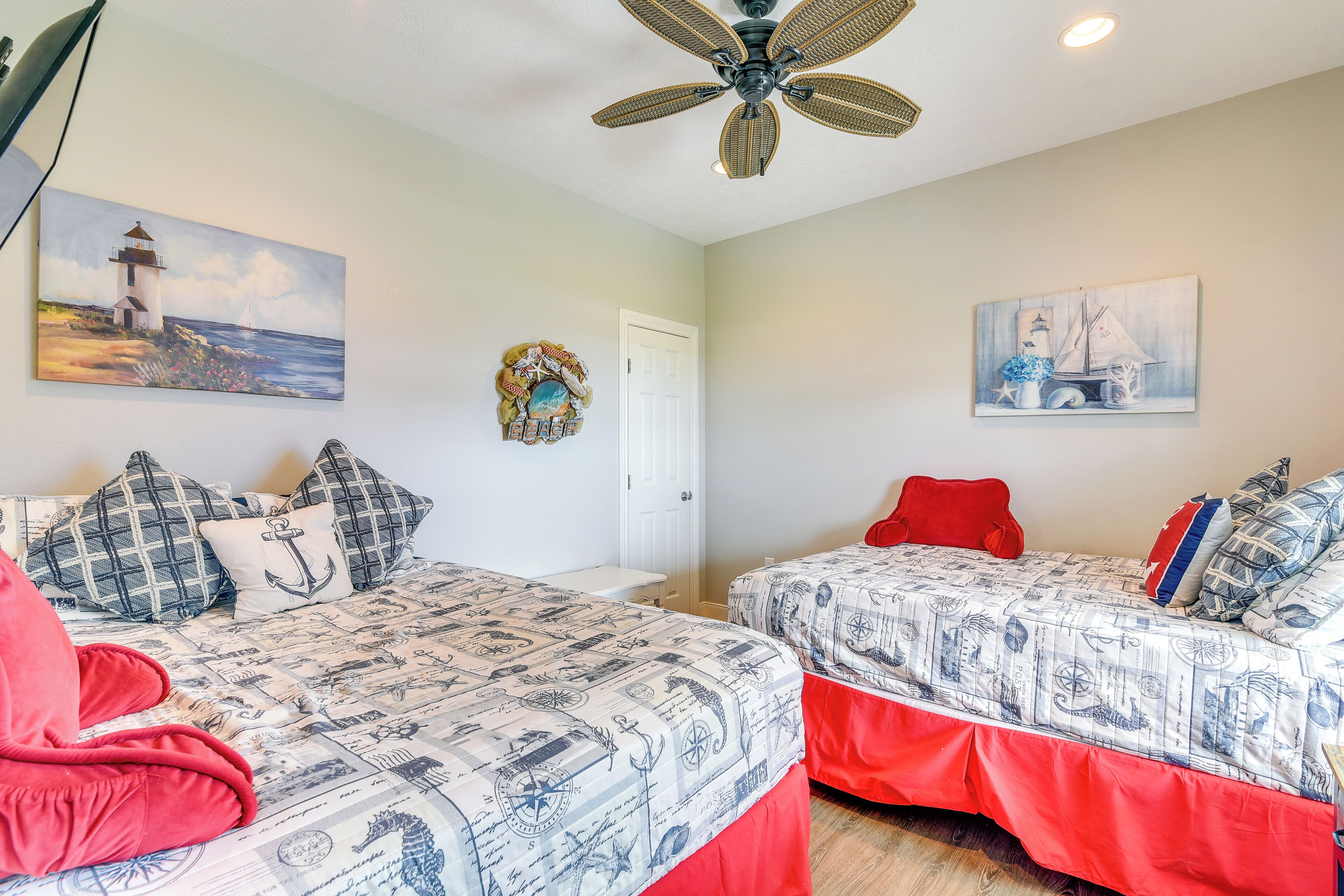 A bedroom with two beds, nautical-themed bedding, a ceiling fan, and maritime artwork on the walls.