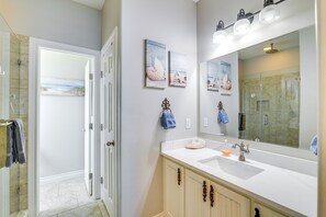 Bathroom features a large mirror, sink, and shower area, with framed artworks and towels on hooks.