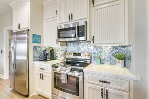 Features a well-lit kitchen with stainless steel appliances, white cabinetry, and a tiled backsplash.
