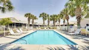 Une piscine avec des chaises longues, des palmiers et une clôture.
