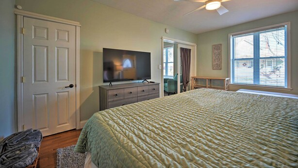 Een slaapkamer met een bed, een televisie op een dressoir, een plafondventilator en een raam met jaloezieën.