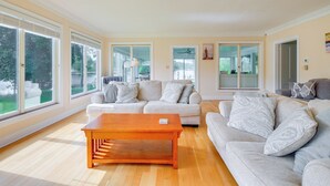A spacious living room with a wooden coffee table, two grey sofas, and large windows offering a view of the outdoors. - 15 Mi to Gloucester: Waterfront Mathews Home! (Mathews)