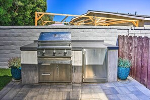 A stainless steel outdoor kitchen with a built-in grill and oven, potted plants, and a wooden fence in the background.