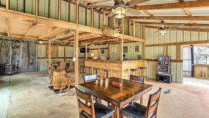 L’intérieur d’une grange rustique, avec une table à manger en bois, des chaises, un coin bar et des ventilateurs de plafond.